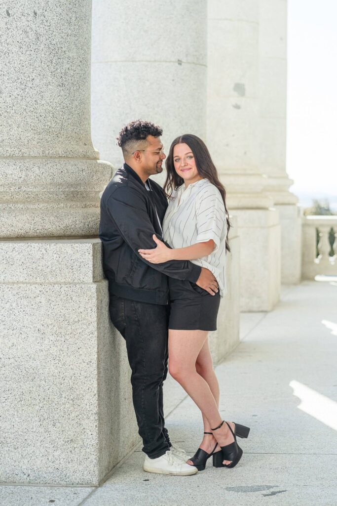a man holds his girlfriend and smiles at her while leaning against a column outside the Utah State Capitol in Salt Lake City