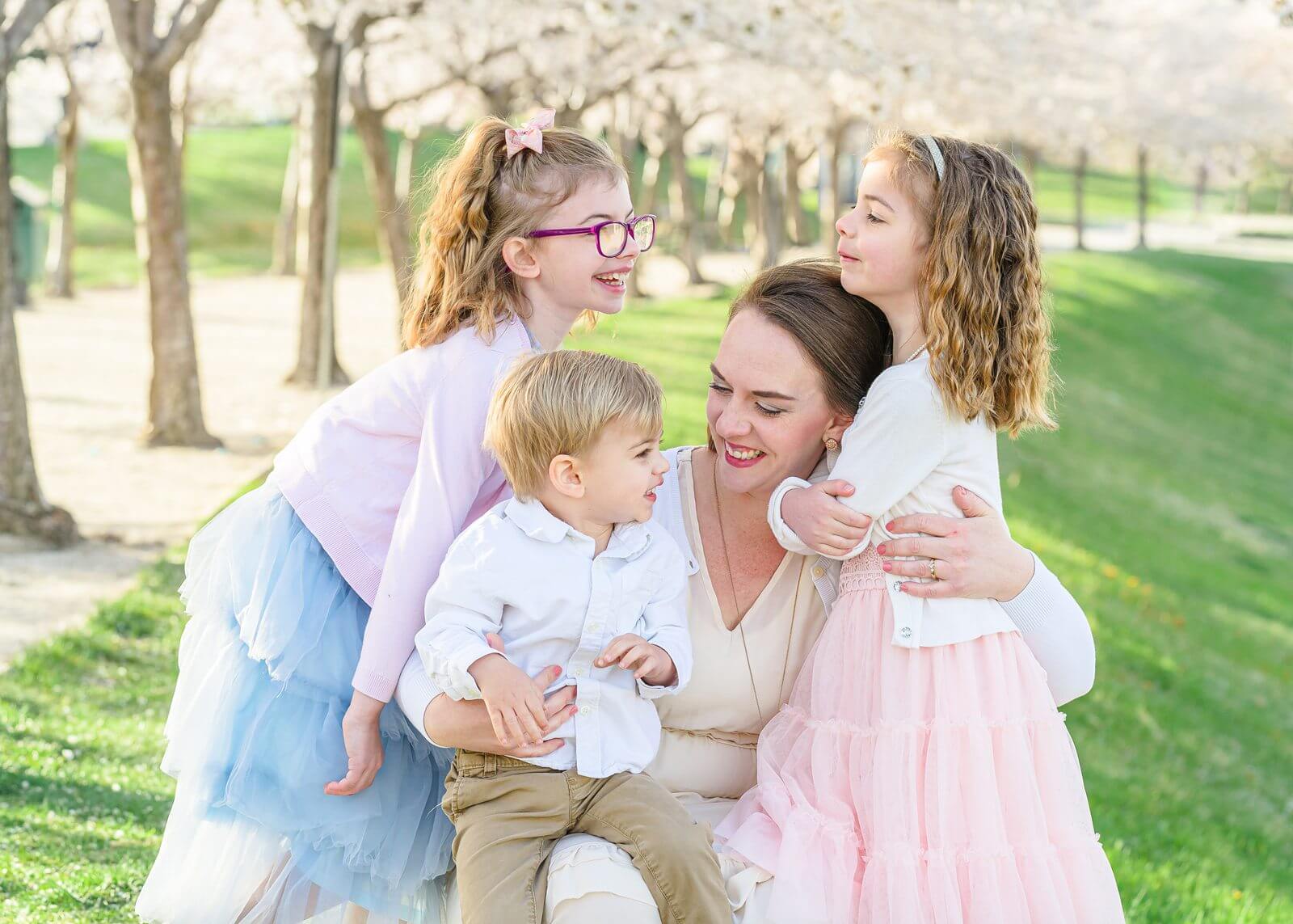 a mother smiles at her two young daughters, and her toddler son for their spring family portrait session at the Utah State Capitol
