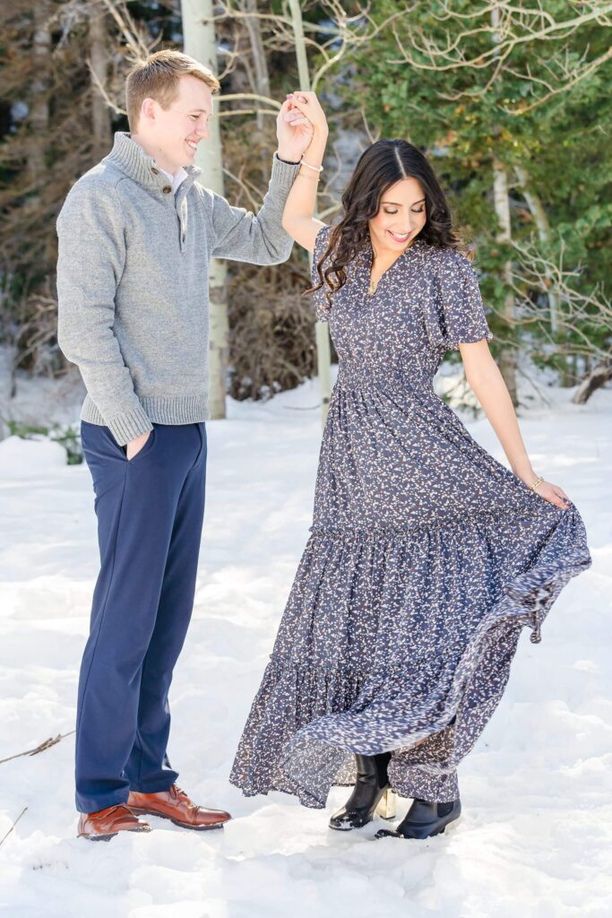A man twirls his fiancee in the snow for their winter engagement session at Aspen Grove in Provo Canyon