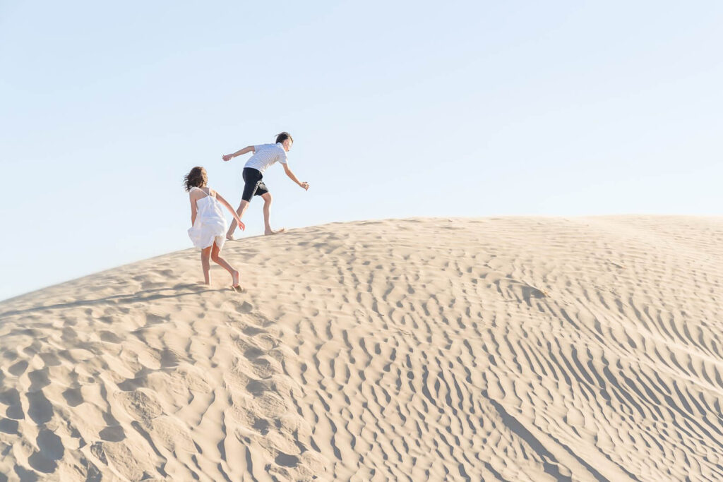 a girl wearing a white sundress and a boy wearing a white polo shirt and black shorts run barefoot up a sand dune in Nephi, Utah