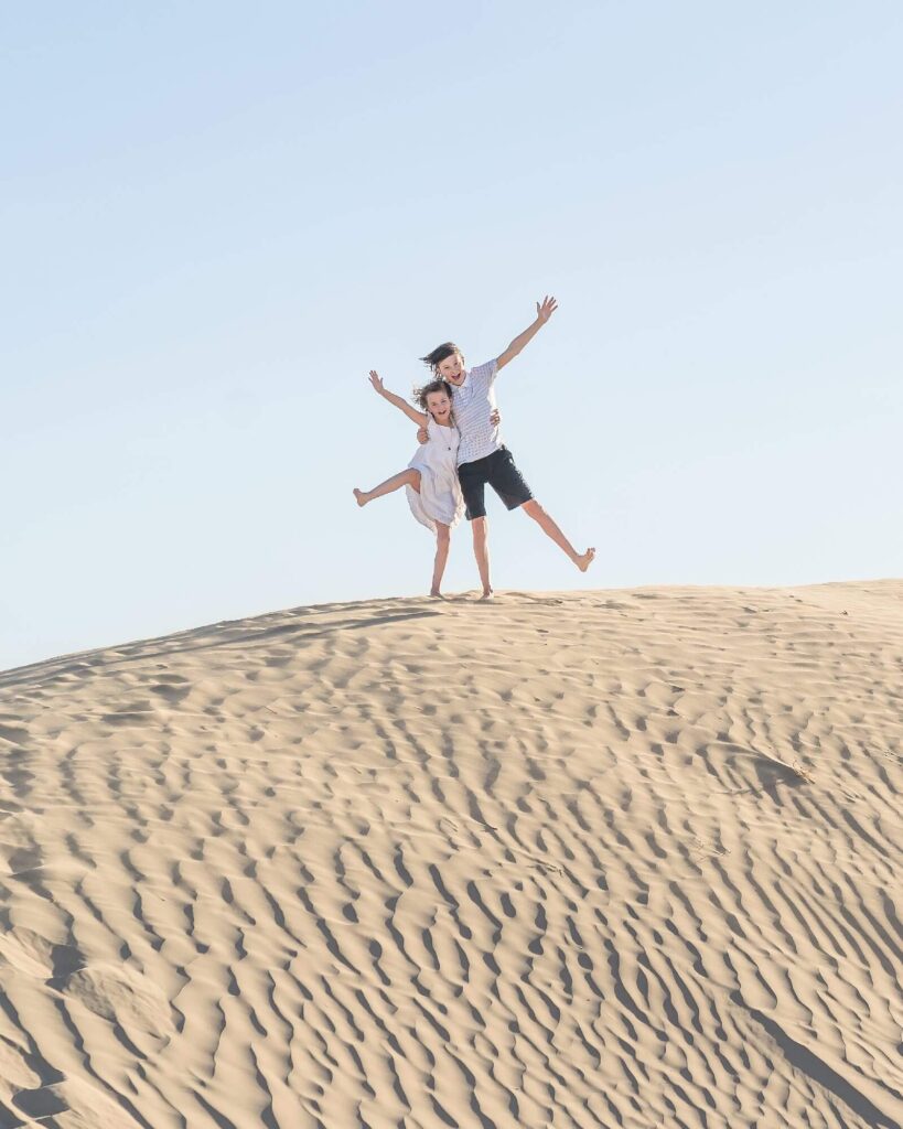 A young girl and a young boy with their arms around each other stand at the top of a sand dune at Little Sahara in Nephi in the summer