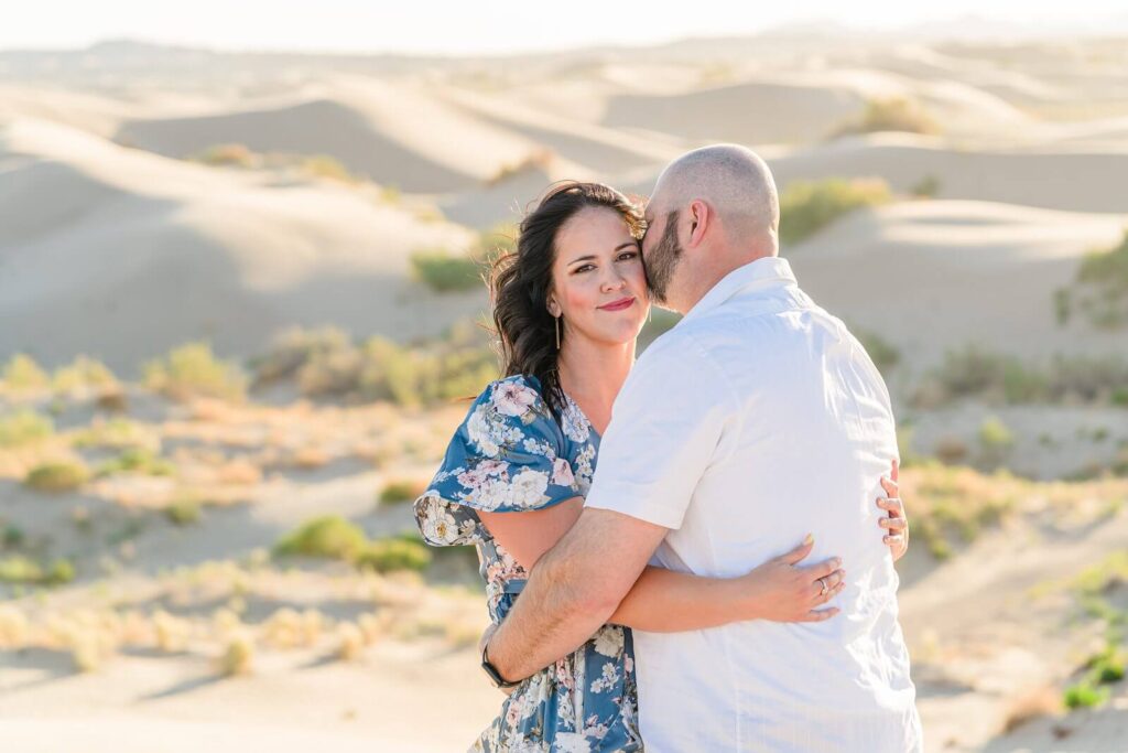 a closeup portrait of a husband and wife embracing with the sand dunes behind them