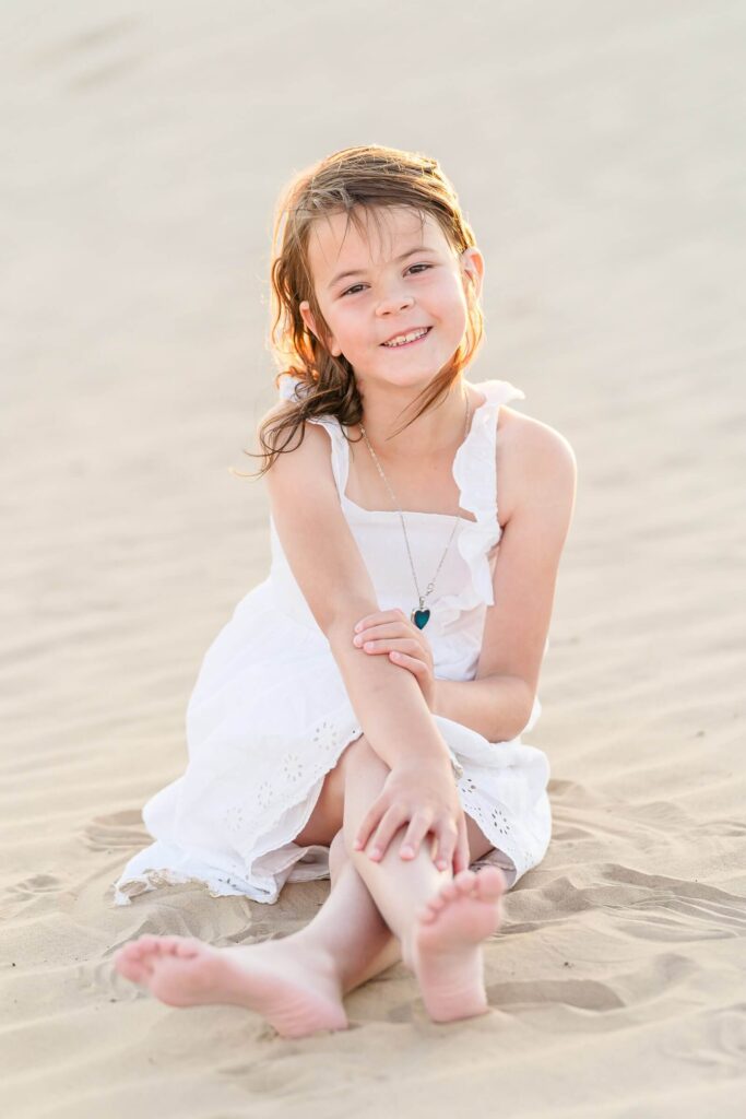 a young girl wearing a white sundress sits in the sand at little sahara, Nephi at sunset