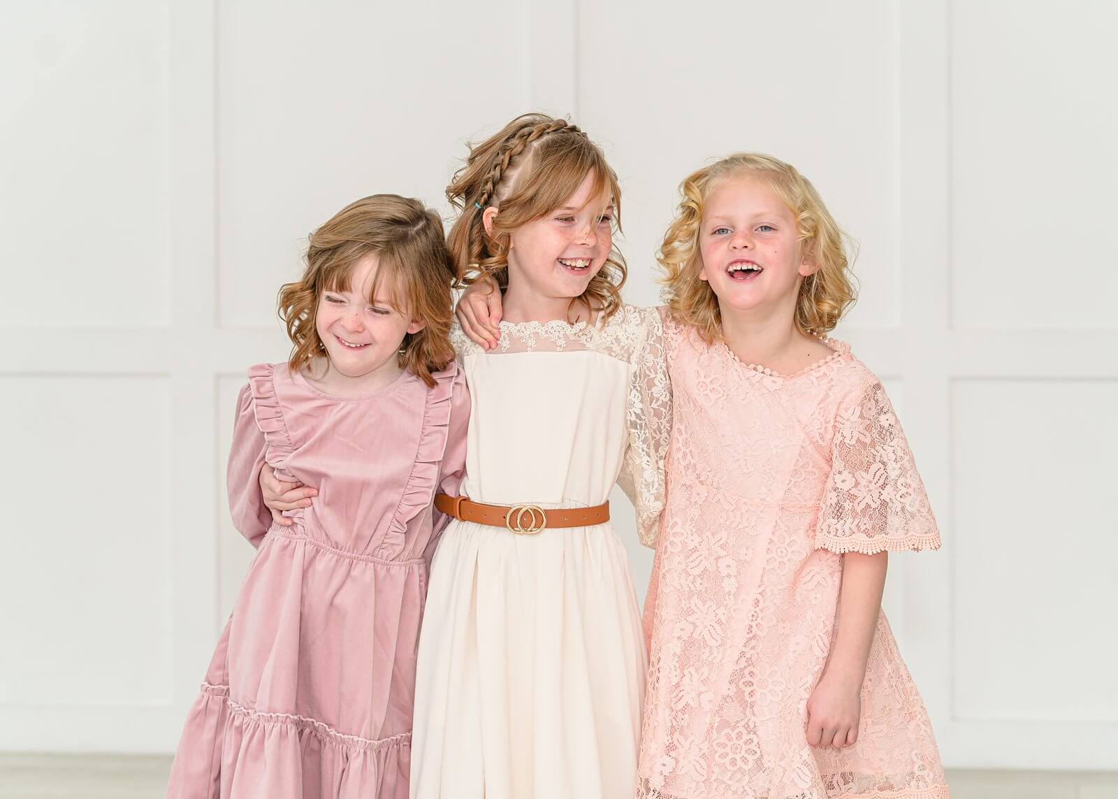 three young girls in pink, cream, and peach colored dresses laugh during their portraits at the Blank Space Studios