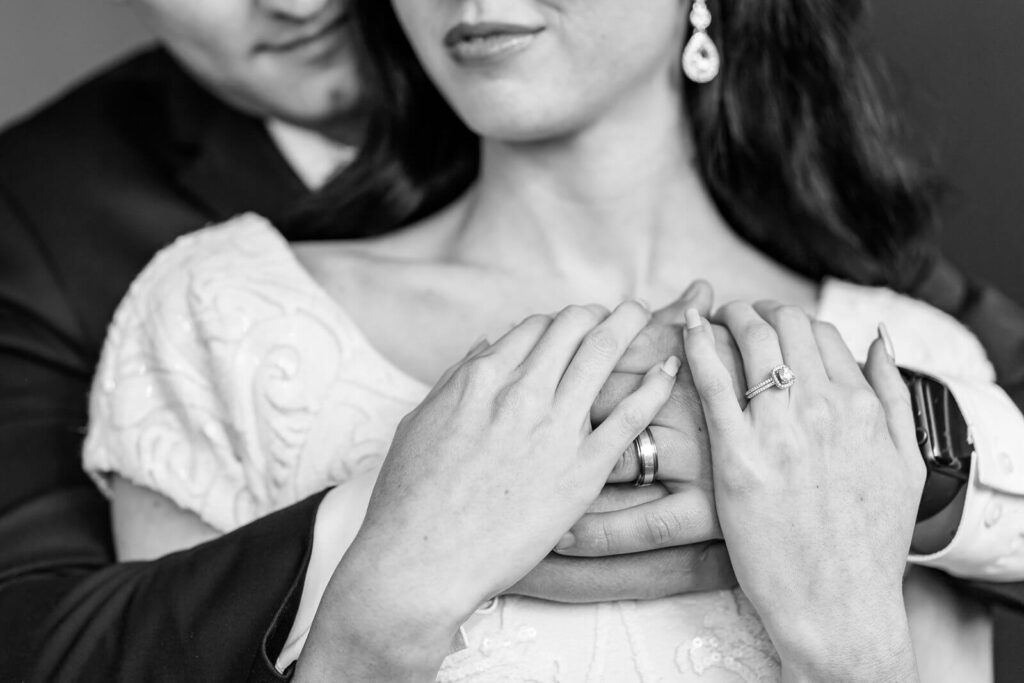 a black and white closeup of a bride's hands holding her groom's hands with both rings visible