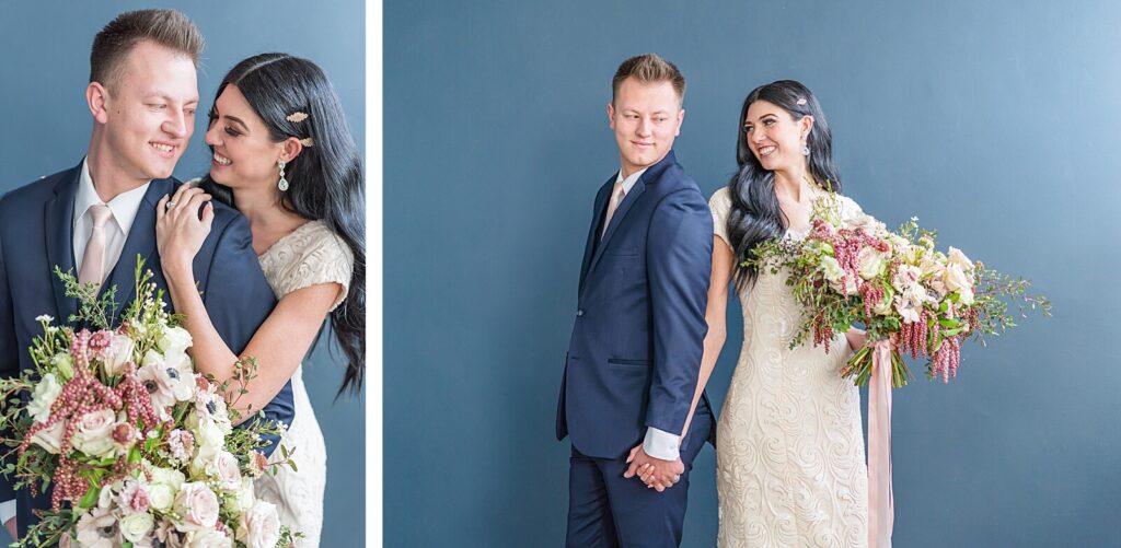 a groom wearing a navy blue suit and a bride wearing a cream colored wedding dress stand shoulder to shoulder holding hands in front of a navy blue wall at Studio Miesh in Salt Lake City