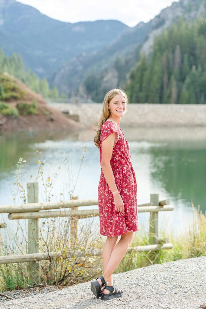 a senior girl from Pleasant grove high school stands in front of a fence with Tibble Fork Reservoir in the background