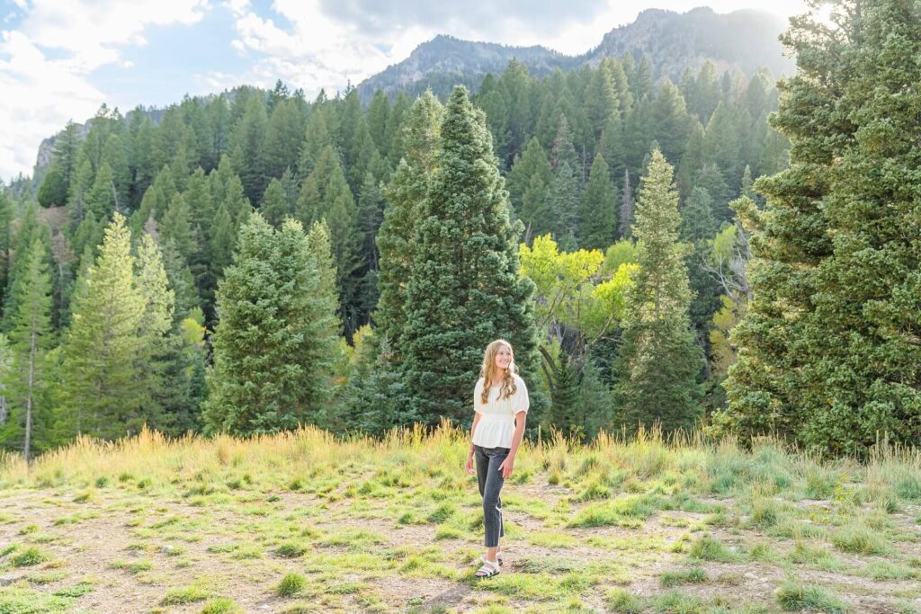 a pleasant grove high school senior girl stands in the grass at Tibble Fork Reservoir with the sun shining down on her