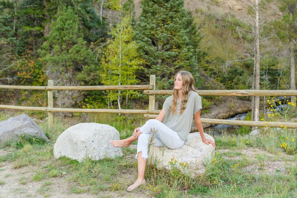 a high school senior girl from pleasant grove sits on a rock with a river in the background