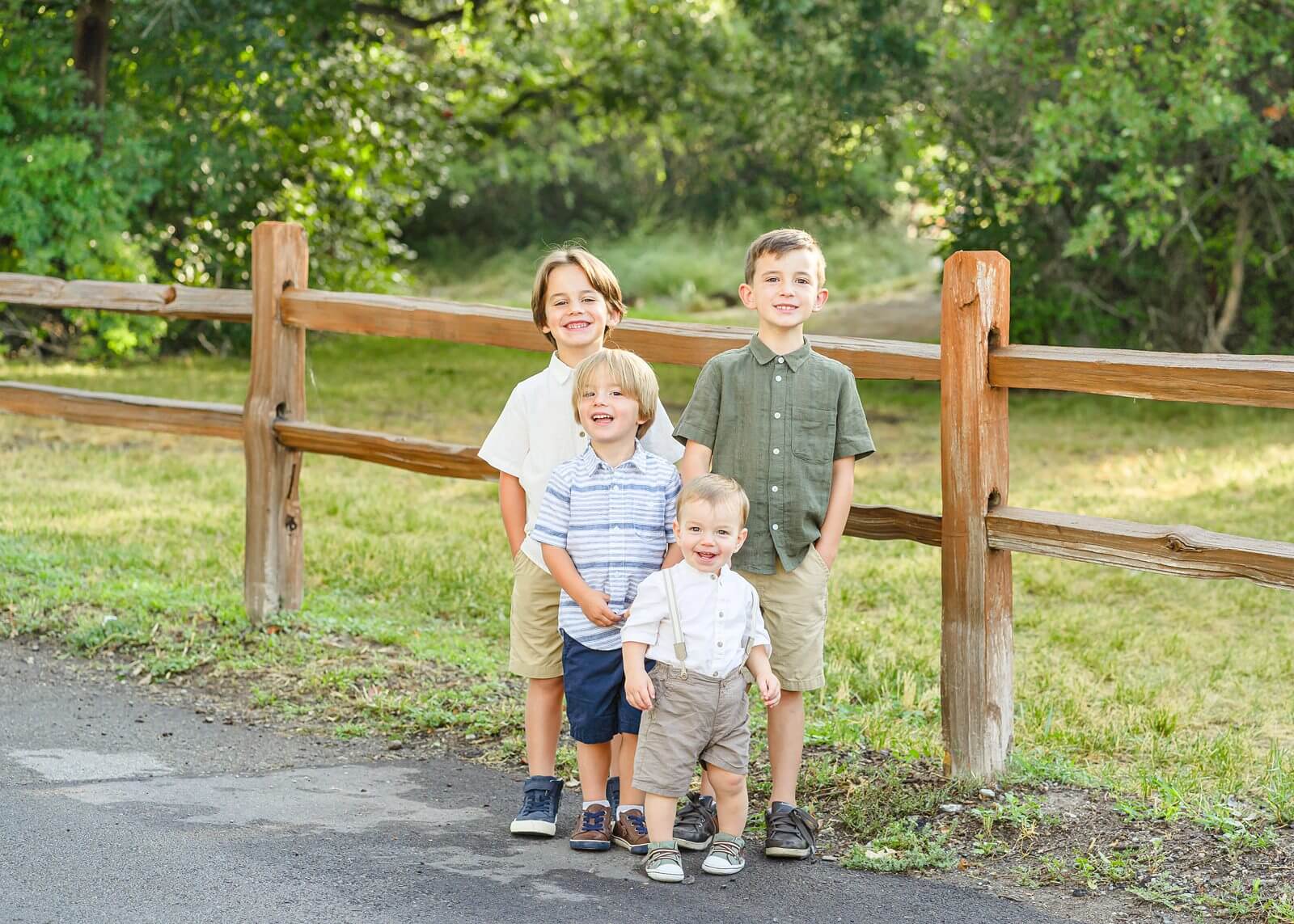 two boys and their toddler brothers stand in front of a wooden fence at Highland Glenn Park in the fall