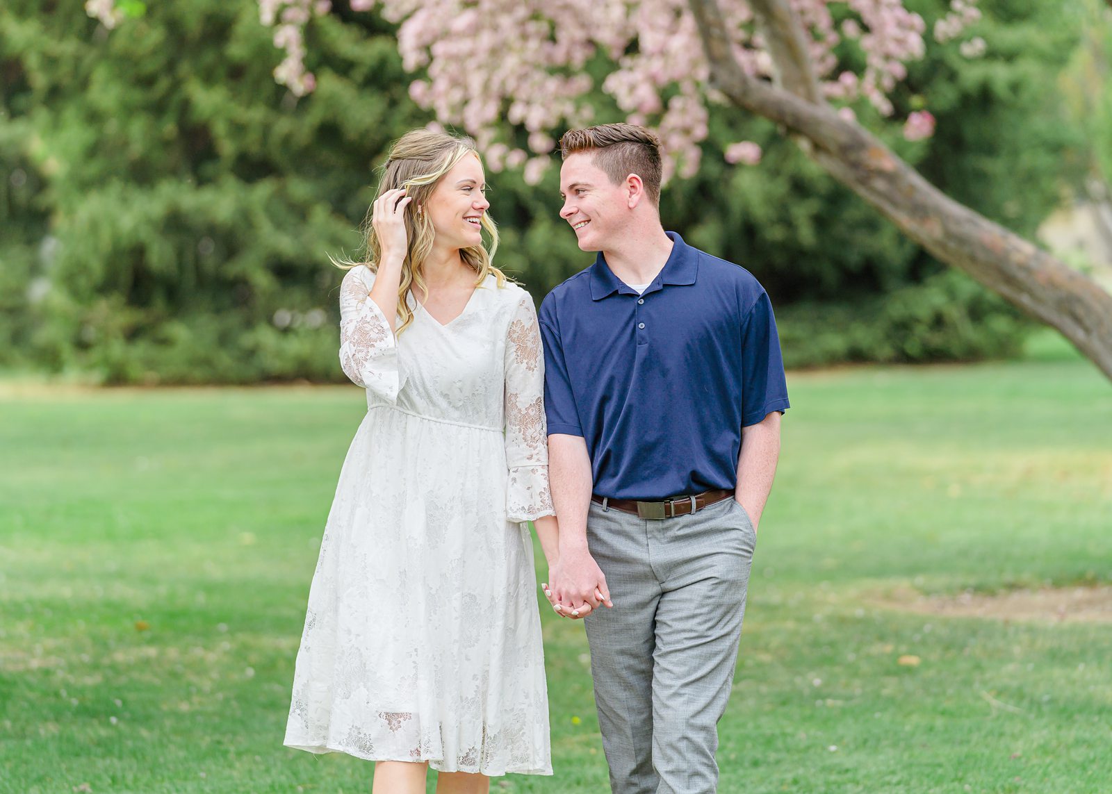 a woman wearing a white lace dress and a man wearing a navy polo shirt and gray slacks holding hands on their date in Utah County