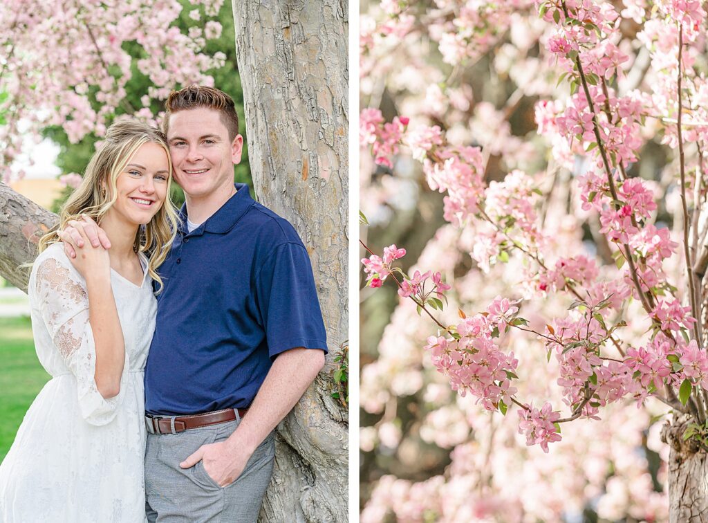 a woman wearing a white lace dress and her fiancé wearing a navy blue polo shirt lean against a blossoming tree in American Fork