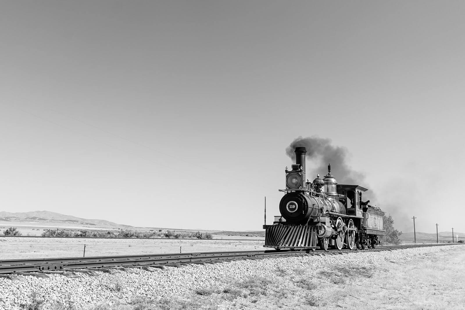 a black and white image of a historical steam engine running along the train tracks towards Golden Spike National Park in Utah